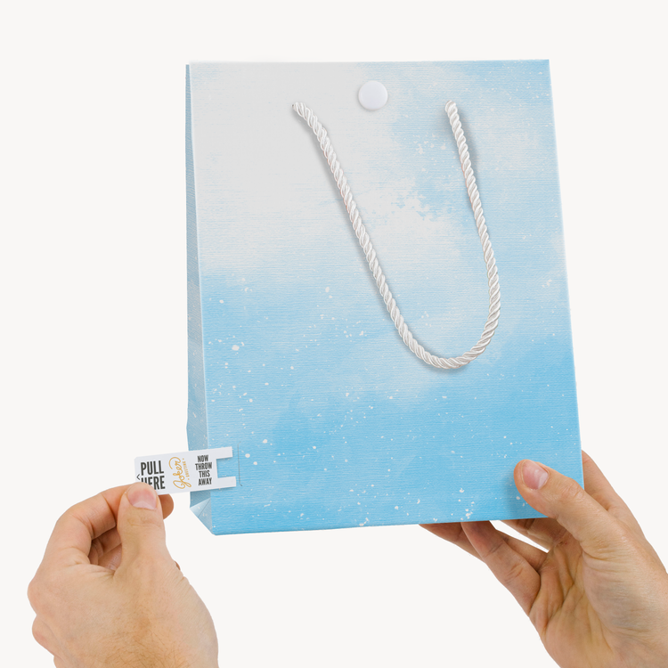 Hands demonstrating Joker Greeting tab removal system on endless Baby Shark musical gift bag with pull tab visible