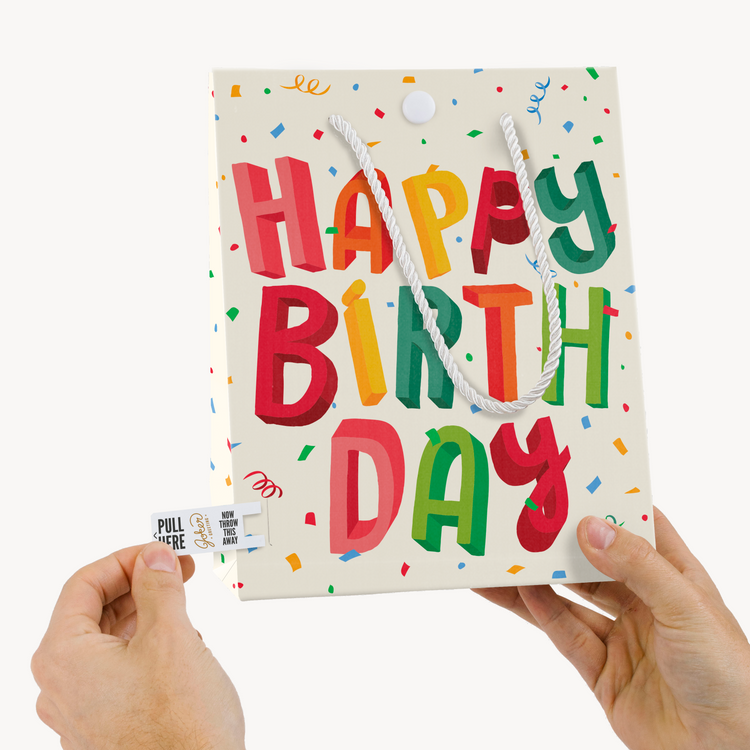 Hands demonstrating Joker Greeting tab removal system on Happy Birthday endless farting musical gift bag with pull tab visible