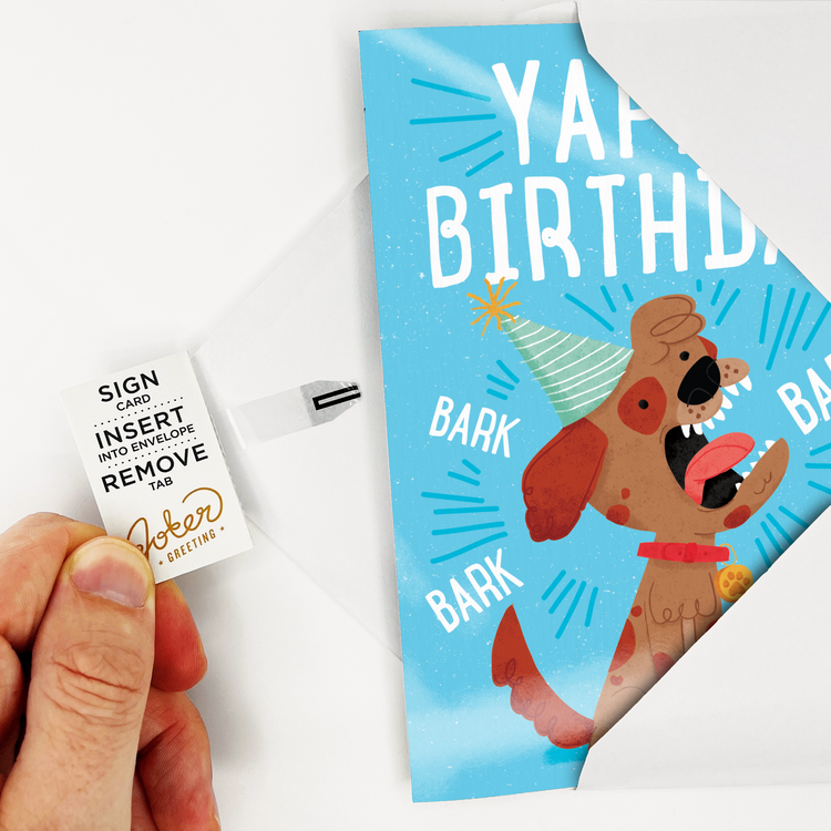 Card with Tab Demonstration:
Hand demonstrating Yappy Birthday dog musical prank card with Joker Greeting instruction tab showing Sign Card Insert Into Envelope Remove Tab activation process