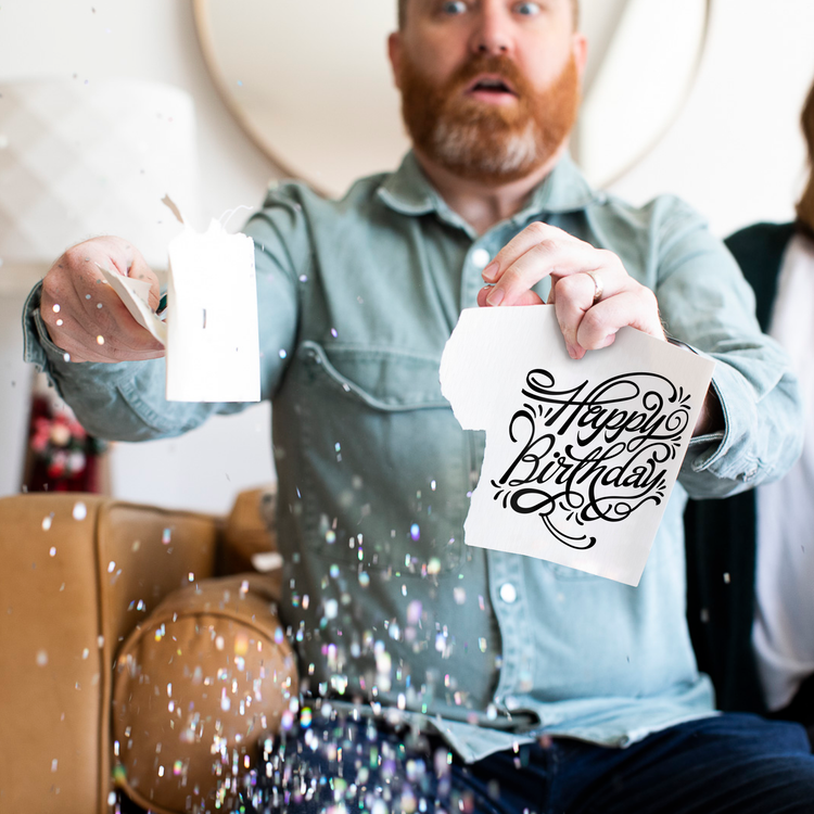 Lifestyle Photo – Man holding torn Joker Greeting birthday card with glitter exploding mid-air, caught in the prank.