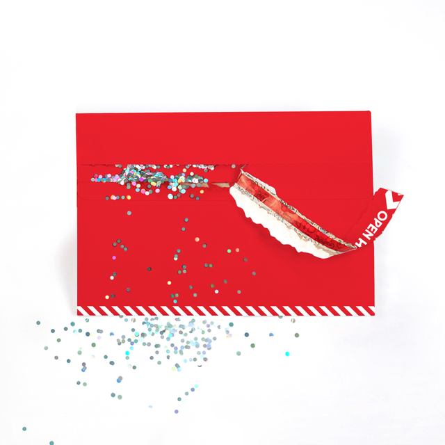 A red envelope with biodegradable glitter spilling out from a strip that was lifted, on a white background.