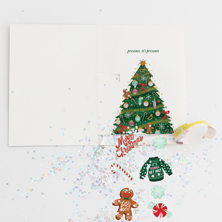 Christmas pull surprise card opened showing large colorful glitter spill and festive stickers including gingerbread man candy cane and ugly sweater designs