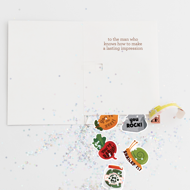 Open Father’s Day greeting card with message “to the man who knows how to make a lasting impression,” surrounded by scattered glitter and colorful pun stickers revealed from a hidden pull tab labeled “pull my finger.”