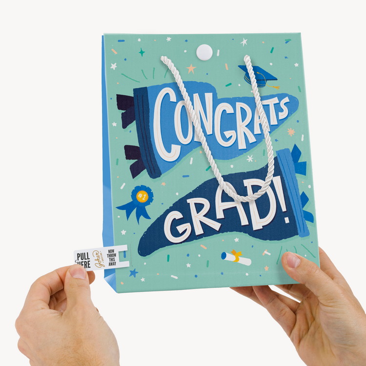 Hands holding Joker Greeting graduation musical bag with pull tab activation system and Congrats Grad celebration theme