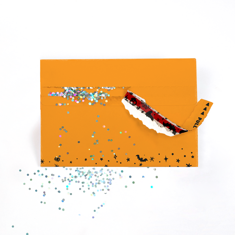 (Envelope being opened with glitter spilling): Orange Halloween glitter trap envelope being opened with colorful glitter spilling out creating spooky prank surprise