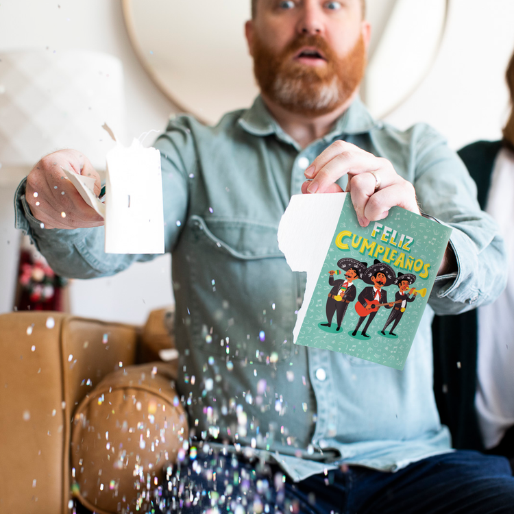 Glitter Action Shot:
Man holding Feliz Cumpleanos mariachi musical prank card with chunky glitter spilling everywhere showing mariachi musicians illustration and glitter defense system by Joker Greeting