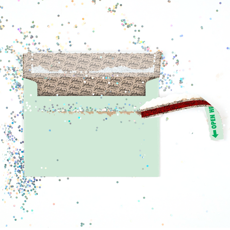 (Final result with glitter scattered): Mint green prank envelope opened with multicolored glitter scattered showing successful fresh-colored glitter trap result