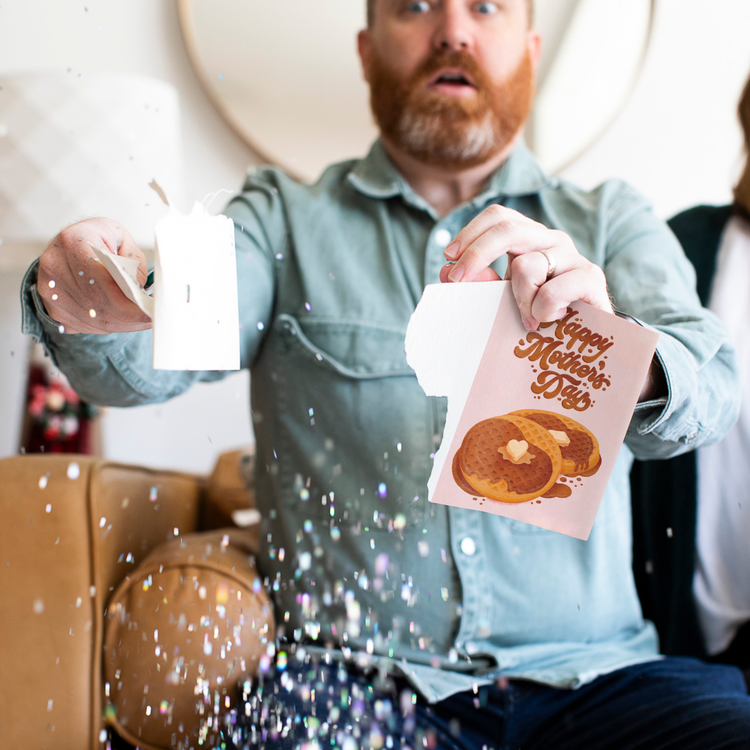 Bearded man holding Never Gonna Give You Up musical Mother's Day card with large glitter falling around him showing activated prank greeting card