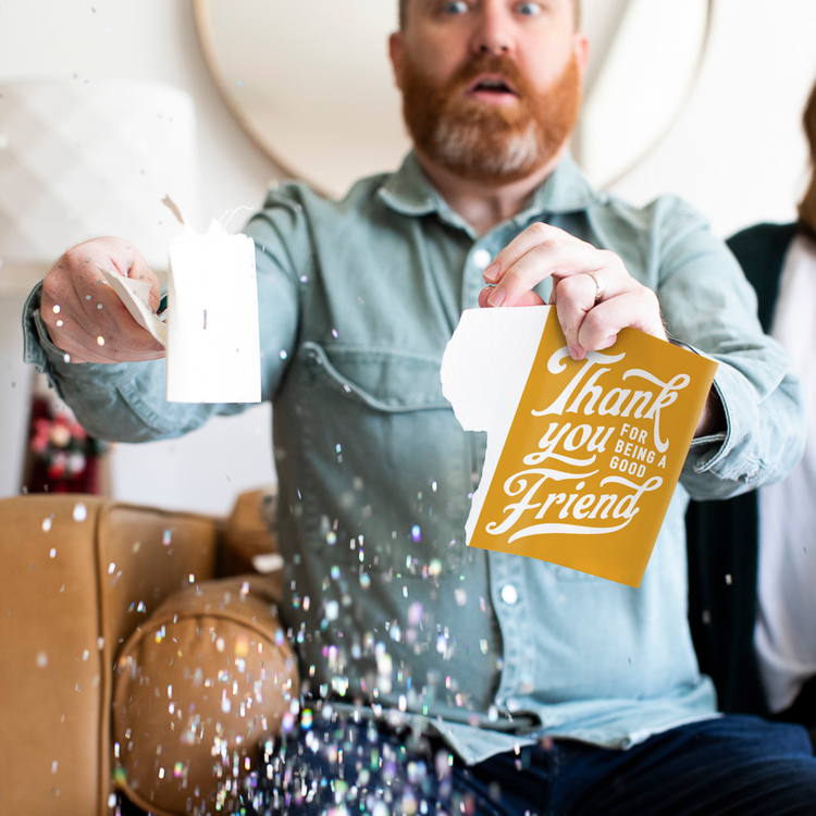 Person holding torn Golden Girls musical greeting card with confetti falling and surprised expression