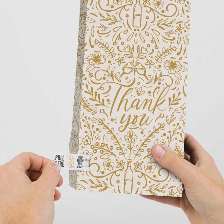 Hands demonstrating tab removal system on elegant gold floral thank you wine gift bag from Joker Greeting endless musical collection
