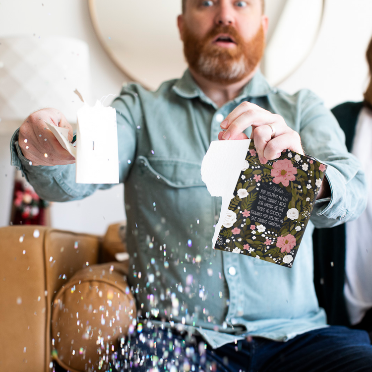 Person holding torn floral musical greeting card with surprised expression as large glitter falls around them