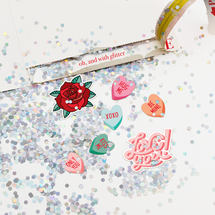 Close-up of opened Joker Greeting Valentine card showing large glitter explosion with romantic heart stickers including hug me only you kiss me and love you messages