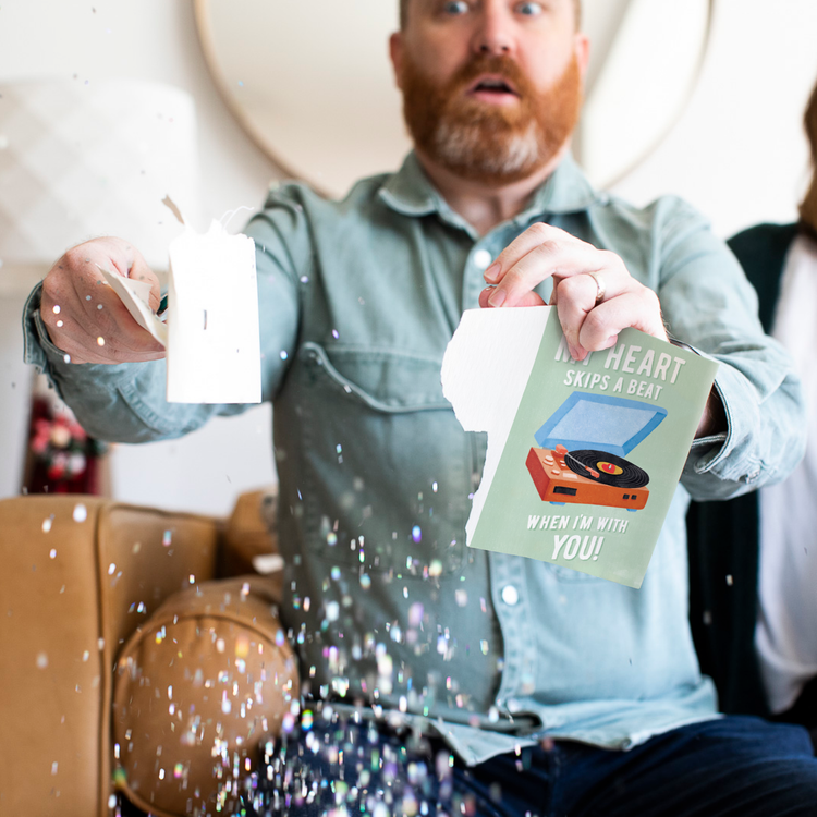 Man holding a mug and a card with confetti falling around him; as he broke the joker greeting card