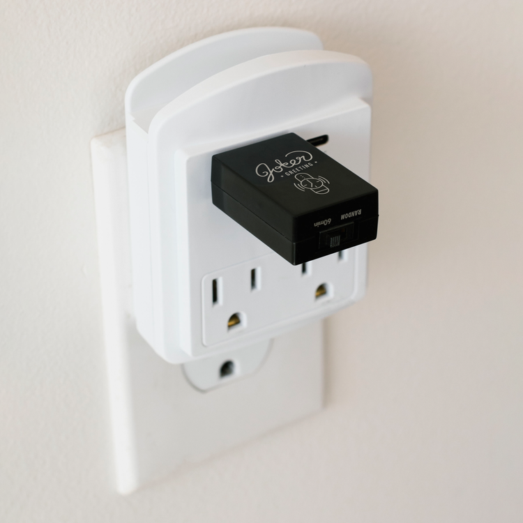 Joker Greeting USB watch beep prank device plugged into white power outlet adapter showing compact stealth installation