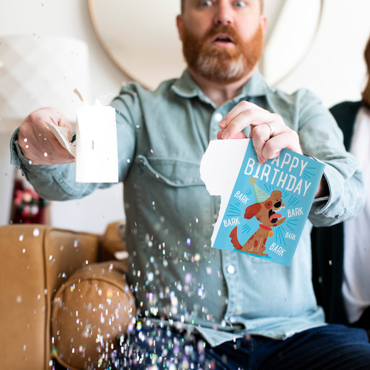 Glitter Action Shot:
Man holding Yappy Birthday dog musical prank card with chunky glitter spilling everywhere showing cartoon dog illustration and barking sound effects design