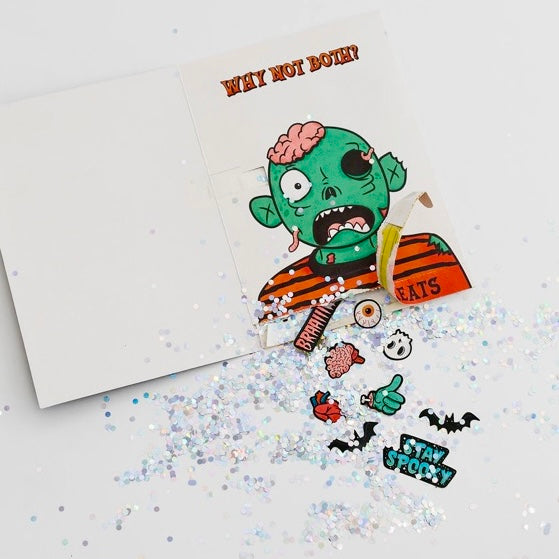 Opened Joker Greeting Halloween prank card showing zombie character with chunky glitter explosion and Halloween stickers scattered around