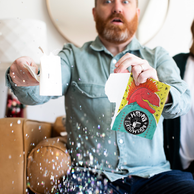 Man opening endless punk rock birthday card with glitter explosion - dinosaur Happy Birthday musical greeting card plays nonstop punk song