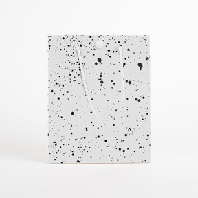 Front view of black speckled musical prank gift bag with button closure and white rope handles