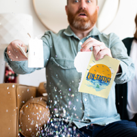 Man holding Fin-Tastic Baby Shark musical glitter card with surprised expression as large glitter sparkles fall around him from Joker Greeting endless collection