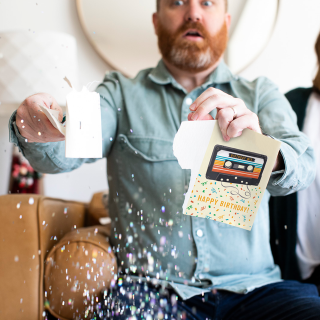 Person opening endless musical birthday greeting card with glitter explosion and surprised expression demonstrating prank activation