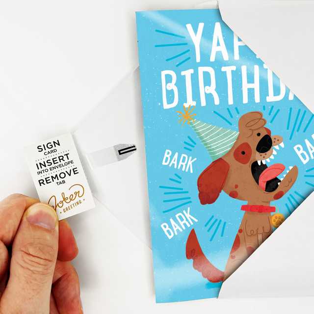 Card with Tab Demonstration:
Hand demonstrating Yappy Birthday dog musical prank card with Joker Greeting instruction tab showing Sign Card Insert Into Envelope Remove Tab activation process