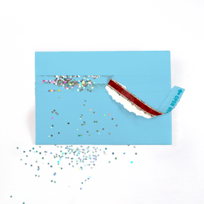 A blue envelope with a strip pulled out, revealing a glitter trap that scattered multicolored glitter around the envelope.