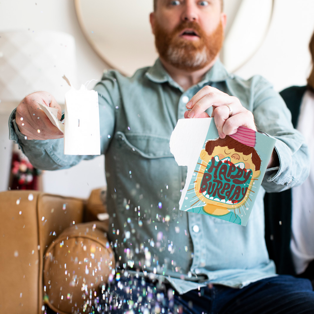 Glitter Action Shot:
Man holding Birthday Burp musical prank card with colorful glitter spilling everywhere demonstrating glitter release when card is broken or tampered with