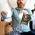 Man holding torn musical Christmas card with glitter explosion showing surprised expression demonstrating glitter feature when card is broken or destroyed