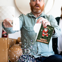 Man holding torn musical Christmas card with glitter explosion showing surprised expression demonstrating glitter feature when card is broken or destroyed