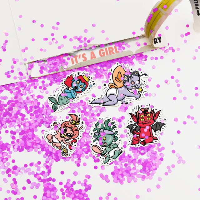 Open gender reveal card revealing IT'S A GIRL message with pink glitter and character stickers including alien, monster, and demon designs