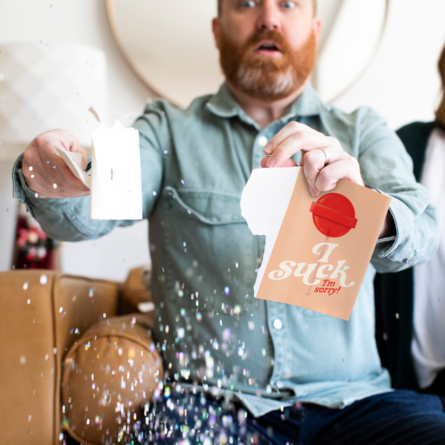 Man holding opened Joker Greeting endless musical sorry card with large glitter explosion effect and surprised facial expression