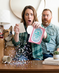 Woman and man in a living room with a dog, reacting to a product they are holding.