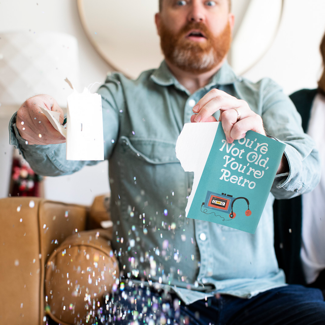 Person opening Joker Greeting endless birthday musical card with glitter explosion and surprised expression showing You're Not Old You're Retro message