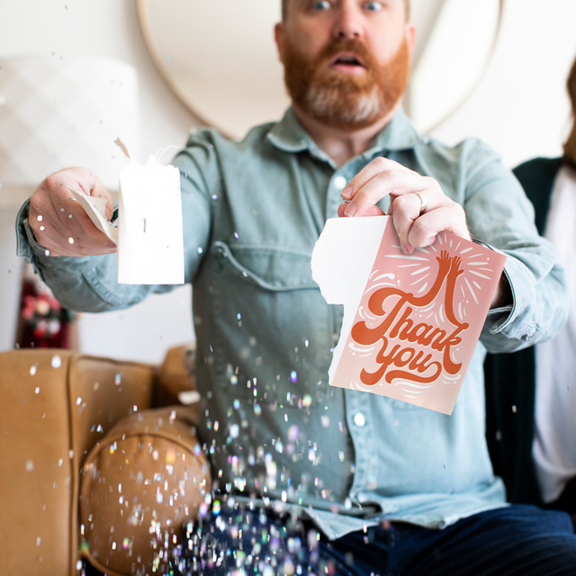 Person holding torn high five thank you card with surprised expression as confetti and glitter falls around them